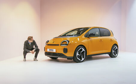 Eine Person hockt in einem Studio neben einem orangenen Renault Twingo 2025, der in einem Studio steht.
