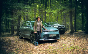 Eine Försterin lehnt an ihrem Auto, das mitten im Wald steht. Dahinter steht ein weiteres Fahrzeug.