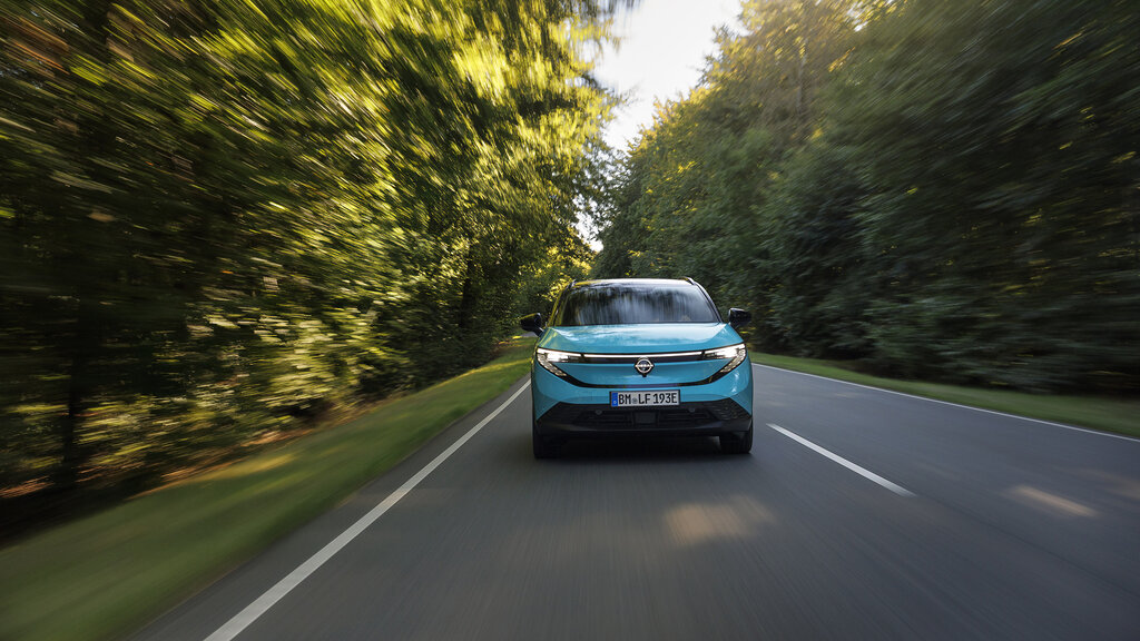 Ein türkiser Nissan Leaf fährt durch einen Wald