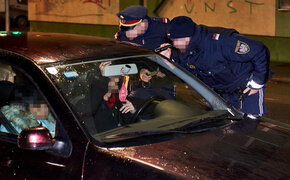 Eine Fahrzeugkontrolle durch zwei Polizisten bei Nacht, sie leuchten mit einer Taschenlampe und kontrollieren den Ausweis des Fahrers. Im Auto sitzen zwei Personen.