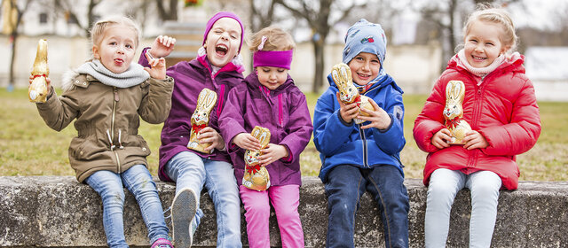 5 Kinder sitzen auf einer Mauer und halten Schokoosterhasen in der Hand auf Schloss Hof.