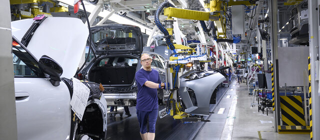Ein blau gekleideter Mann arbeitet am Fließband in einer Autofabrik                   