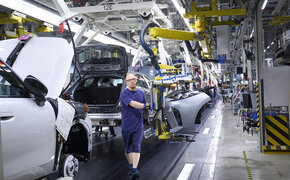 Ein blau gekleideter Mann arbeitet am Fließband in einer Autofabrik                   