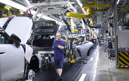 Ein blau gekleideter Mann arbeitet am Fließband in einer Autofabrik                   