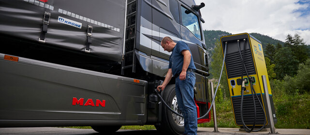 Ein Mann steckt einen Lkw an einer Ladesäule an