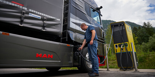 Ein Mann steckt einen Lkw an einer Ladesäule an