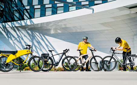 Vier Pedelecs stehen aufgereiht vor einem Gebäude. Mit im Bild sind auch zwei auto touring-Redakteure.