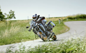Die Reisenduro fährt in Schräglage eine Rechtskurve auf einer Landstraße entlang.