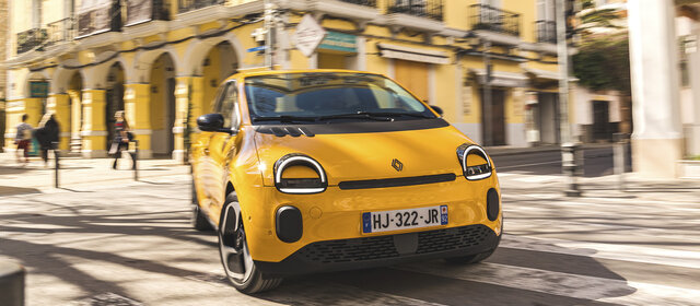 Ein gelber Renault Twingo fährt um eine Kurve in der Stadt.