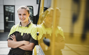 Frau in Arbeitskleidung steht vor einem gelben Kraftfahrzeug. Sie ist ÖAMTC-Pannenhelferin