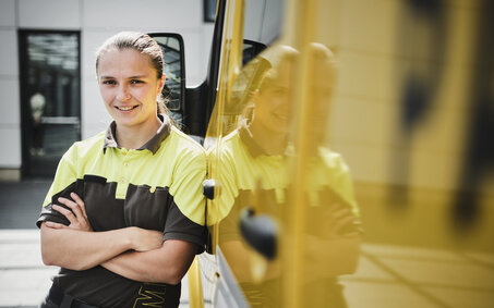 Frau in Arbeitskleidung steht vor einem gelben Kraftfahrzeug. Sie ist ÖAMTC-Pannenhelferin