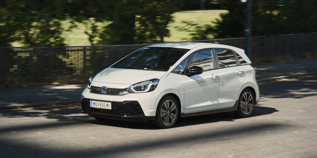 Ein weißer Honda Jazz fährt an einem Park vorbei