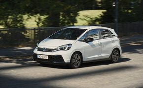Ein weißer Honda Jazz fährt an einem Park vorbei