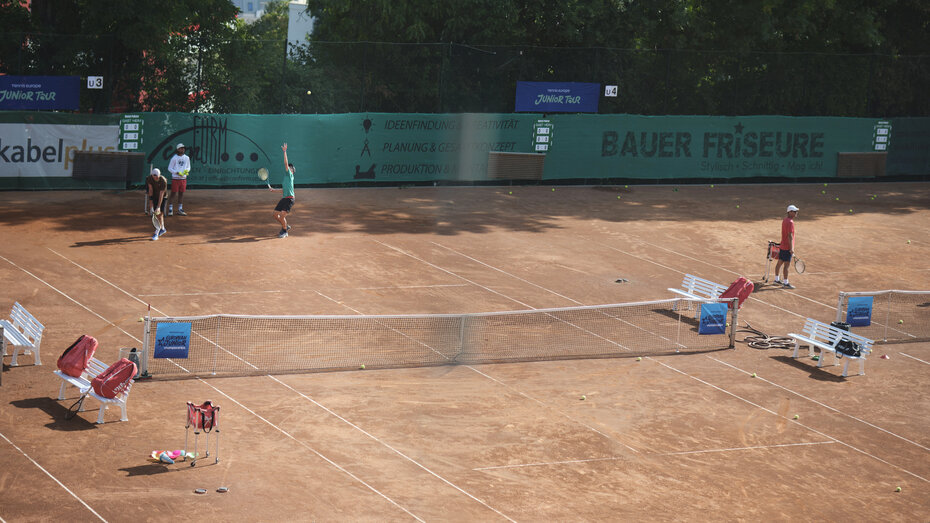 Auf einem Tennis-Sandplatz schlägt ein Spieler in grünem T-Shirt auf,