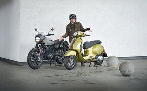 Mann mit fragender Gestik steht zwischen Motorrad und Roller 