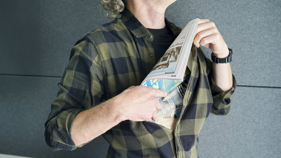 Ein Mann (Kopf nicht sichtbar) stopft eine Zeitung unter sein kariertes Hemd.