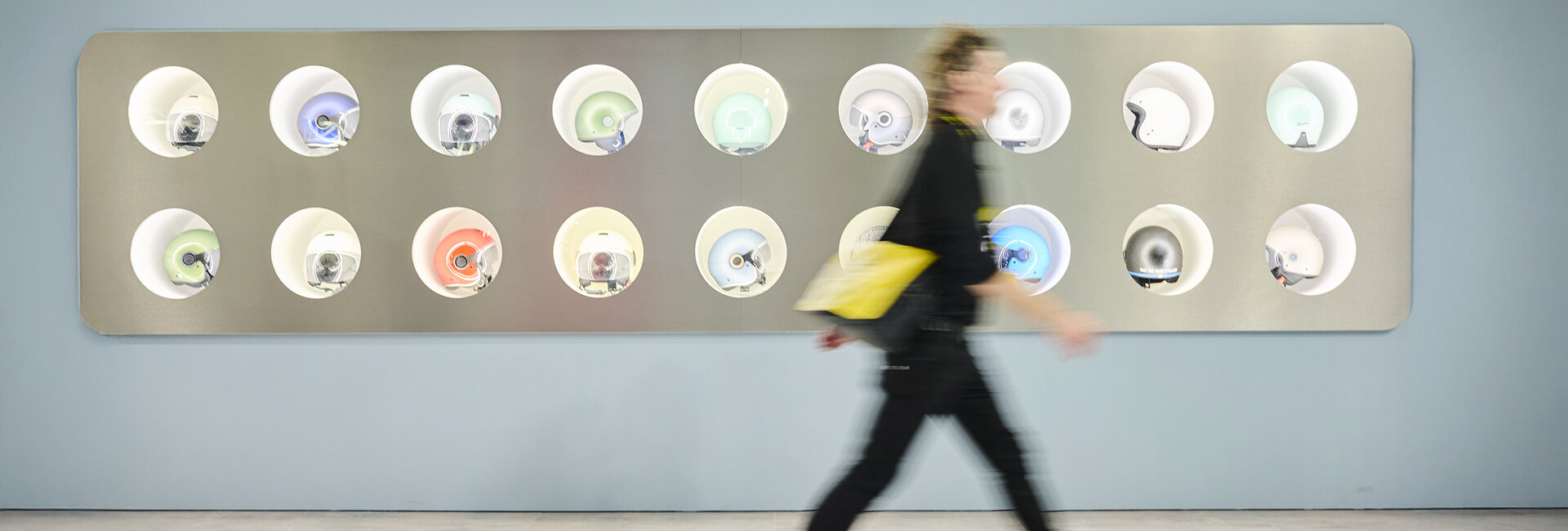 Mann geht an einer Wand voller Motorradhelme vorbei.