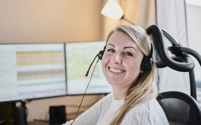 Eine blonde Frau (Victoria Rödleithner) mit Headset zum Telefonieren sitzt vor einem Computer und lacht.
