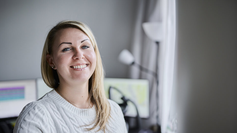 Eine blonde Frau (Victoria Rödleithner) lächelt in die Kamera, im Hintergrund sind Bildschirme zu sehen.