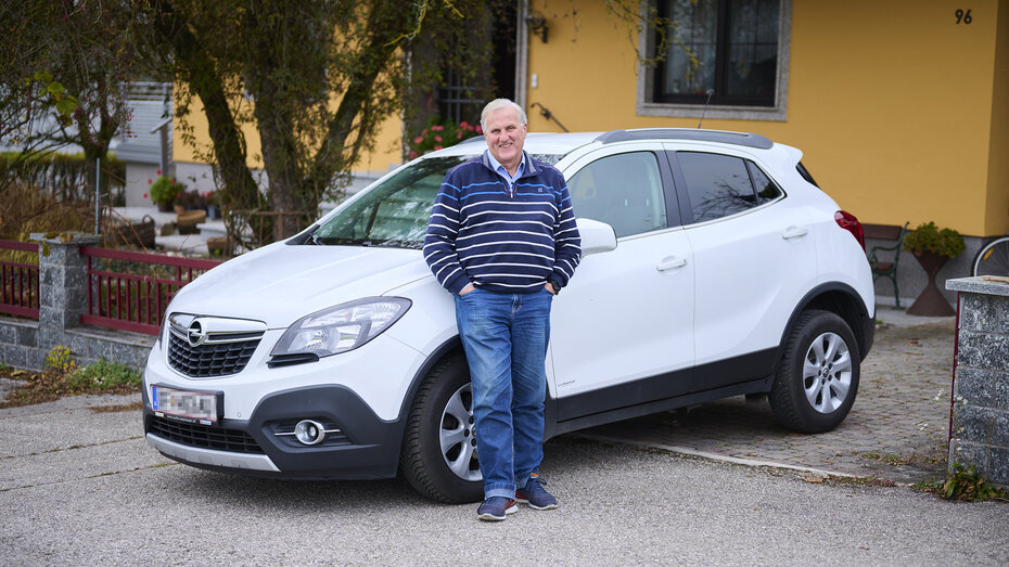 Ein langjähriges ÖAMTC-Mitglied steht vor seinem Auto, einem weißen Opel