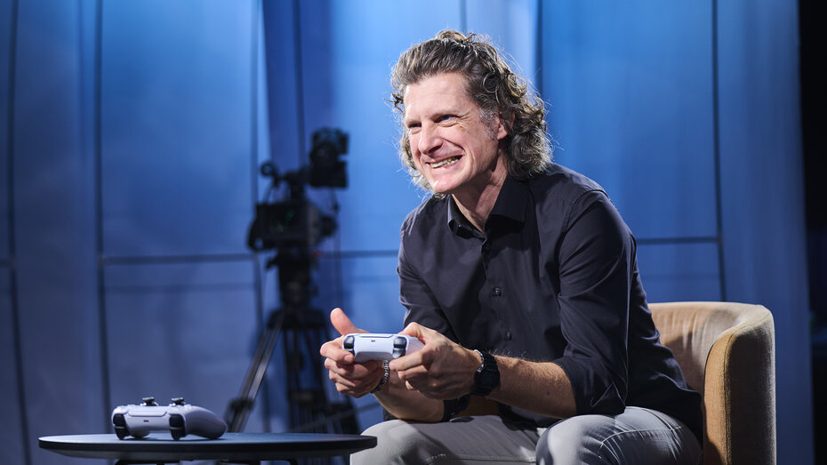 Redakteur Alex Fischer sitzt mit PS5 Controller und spielt. Er lacht. 
