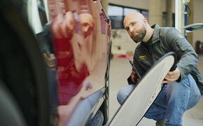 Ein Schadensbegutachter prüft mit einem Dellenspiegel die Tür eines roten Fahrzeugs.