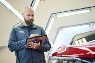 Ein Schadensbegutachter gibt in sein Tablett die Daten eines roten Fahrzeugs ein.