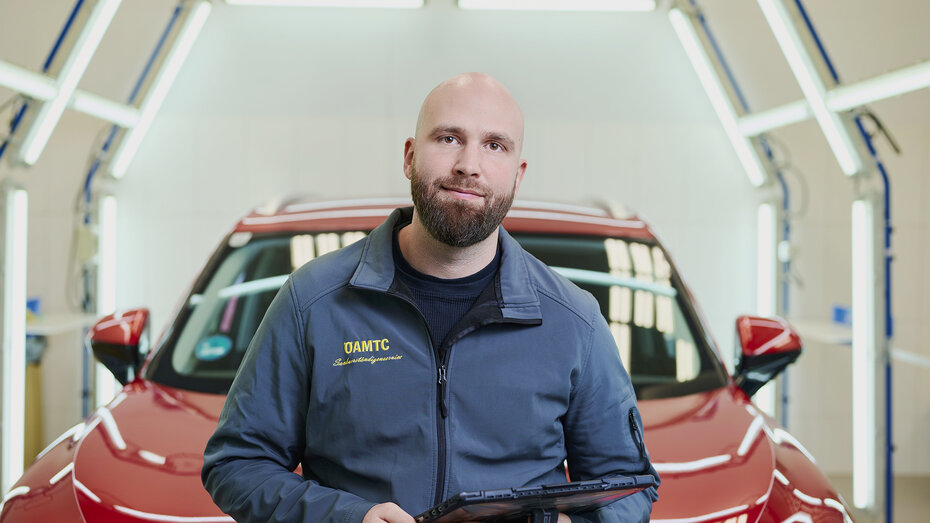 Ein Schadensbegutachter David Kaiser steht im Lichttunnel am ÖAMTC-Stützpunkt vor einem roten Auto.