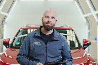 Ein Schadensbegutachter David Kaiser steht im Lichttunnel am ÖAMTC-Stützpunkt vor einem roten Auto.