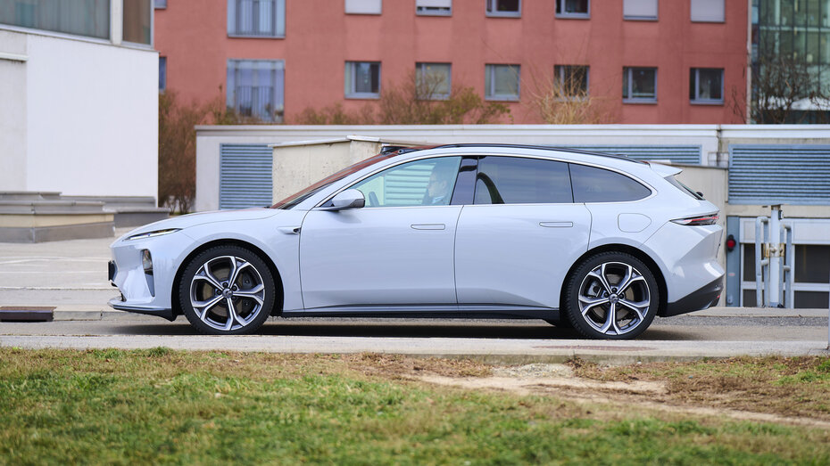 Ein hellblauer Nio ET5 Touring steht auf einer Straße durch einen urbanen Raum, im Hintergrund befindet sich ein rotes Geböude.