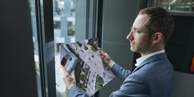 Verkehrsexperte Matthias Nagler steht vor einem Fenster und hält eine Karte in der Hand.