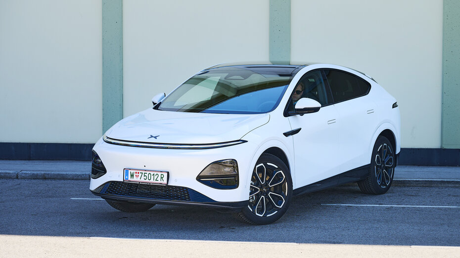 Ein weißer Xpeng G6 steht quer auf der Straße vor einer leicht grünen Wand.