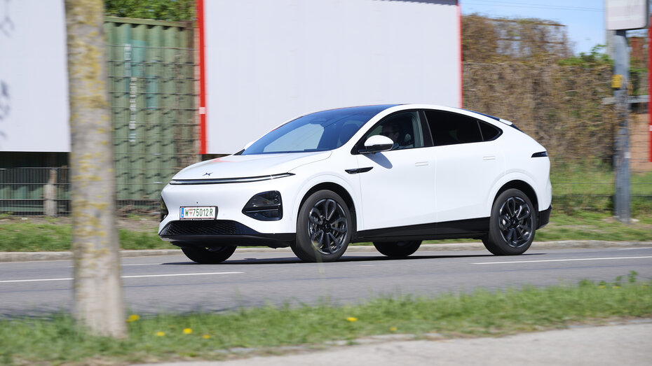 Ein weißer Xpeng G6 fährt auf einer Straße vor einer weißen Plakatwand.