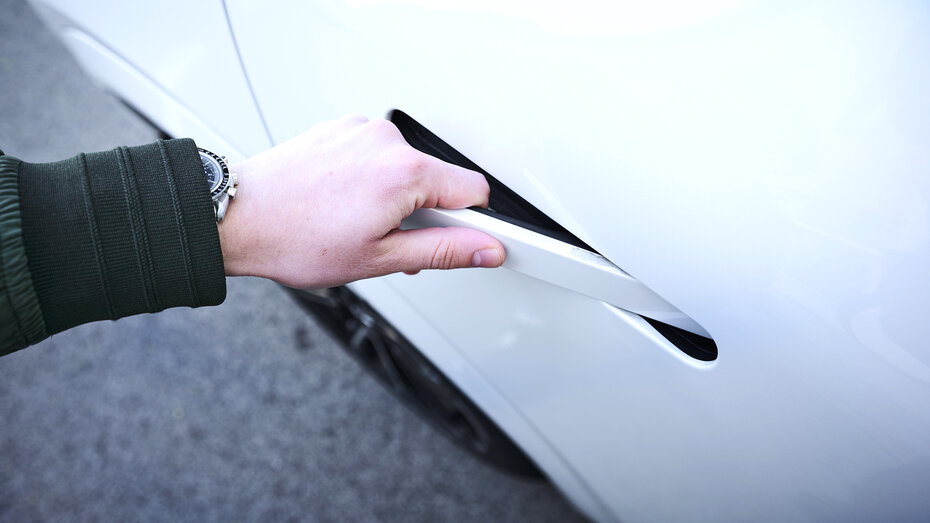 Eine Person greift zum Türgriff eines weißen Autos.