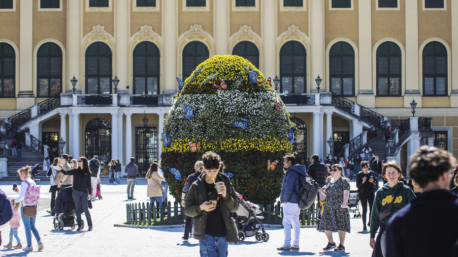 Verschiedene Menschen befinden sich vor einem großen Busch in Ostereiform am Platz vor dem Schloss Schönbrunn.