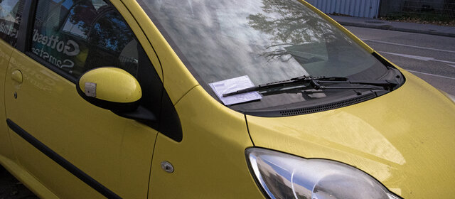 In der Winschutzscheibe eines Autos steckt ein Strafzettel hinter dem Scheibenwischer