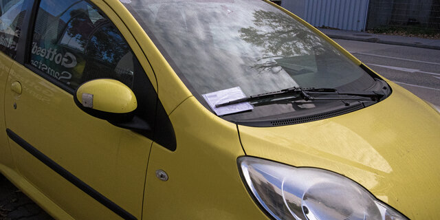 In der Winschutzscheibe eines Autos steckt ein Strafzettel hinter dem Scheibenwischer