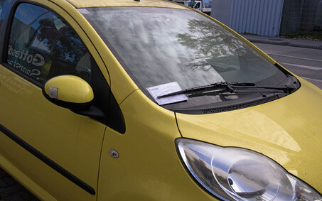 In der Winschutzscheibe eines Autos steckt ein Strafzettel hinter dem Scheibenwischer