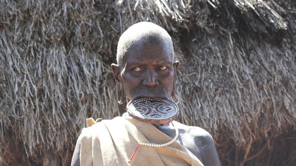 Ein Afrikaner mit Tellerlippe vor einer Hütte.