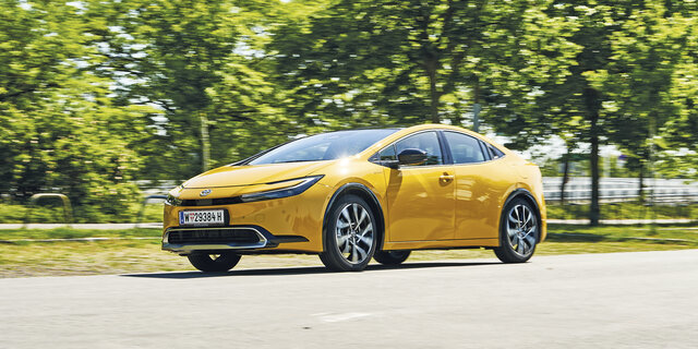 Fahrender Toyota Prius in grüner Landschaft.