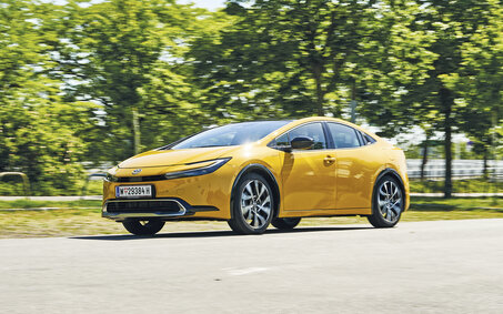 Fahrender Toyota Prius in grüner Landschaft.