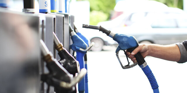 Eine Hand nimmt den Tankstutzen in die Hand an einer Tankstelle.