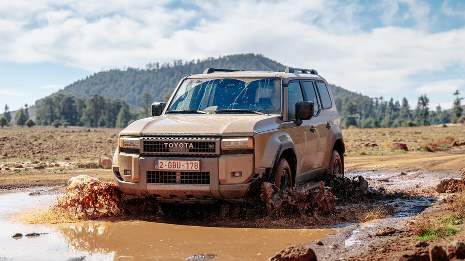 Ein braunes Geländeauto fährt durch eine große Wasserlacke. 