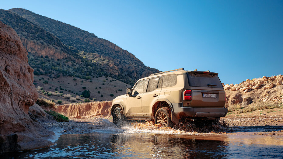 Ein brauner Geländewagen fährt durch eine große Wasserlacke.