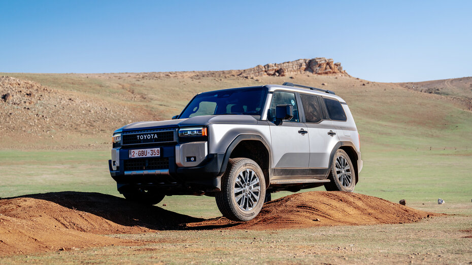 Ein Geländeauto fährt über einen Hügel, wodurch das linke Vorderrad komplett in der Luft steht.