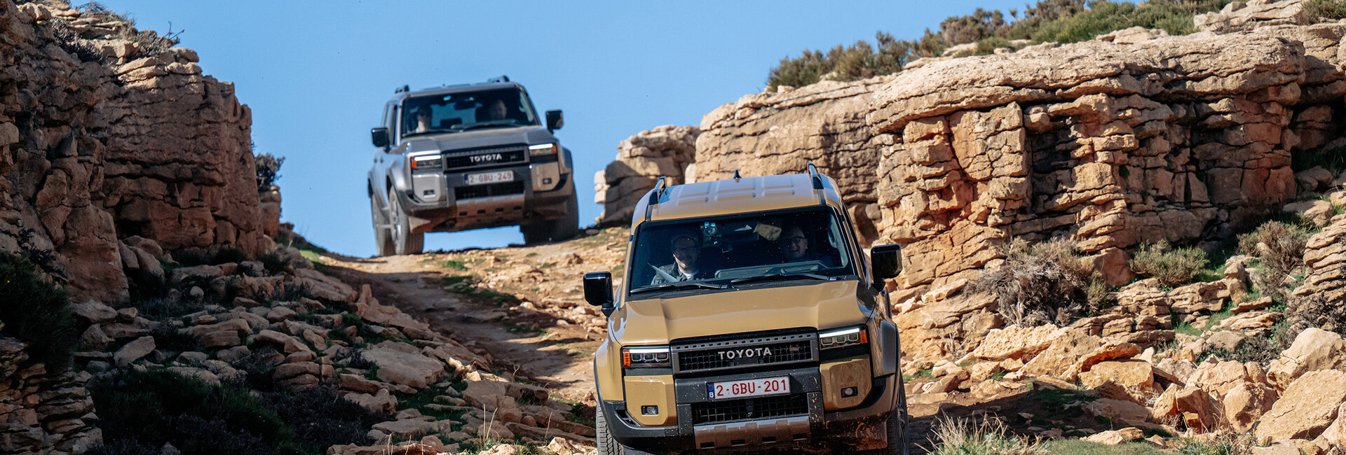 Zwei Geländeautos fahren über einen steinigen Weg.