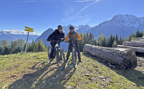Ein Frau und ein Mann posieren am E-Bike lachend. Im Hintergrund die Berge