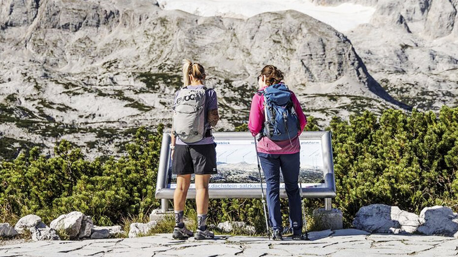 Zwei Wanderer stehen vor einer Informationstafel.