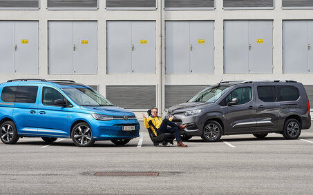 Im Bild sieht man links einen hellblauen VW Caddy und rechts einen dunkelblauen Toyota Proace City Verso, zwischen den beiden sitzt ein auto touring-Redakteur.