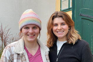 Zwei Frauen, eine mit Haube, stehen vor einem Haus. Es sind die Parasportlerinnen Vroni und Elisabeth Aigner.